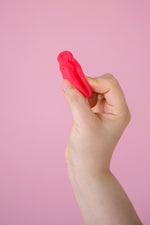 Hey Girls Large red Silicone Menstrual Cup held in someone's hand on a pink background