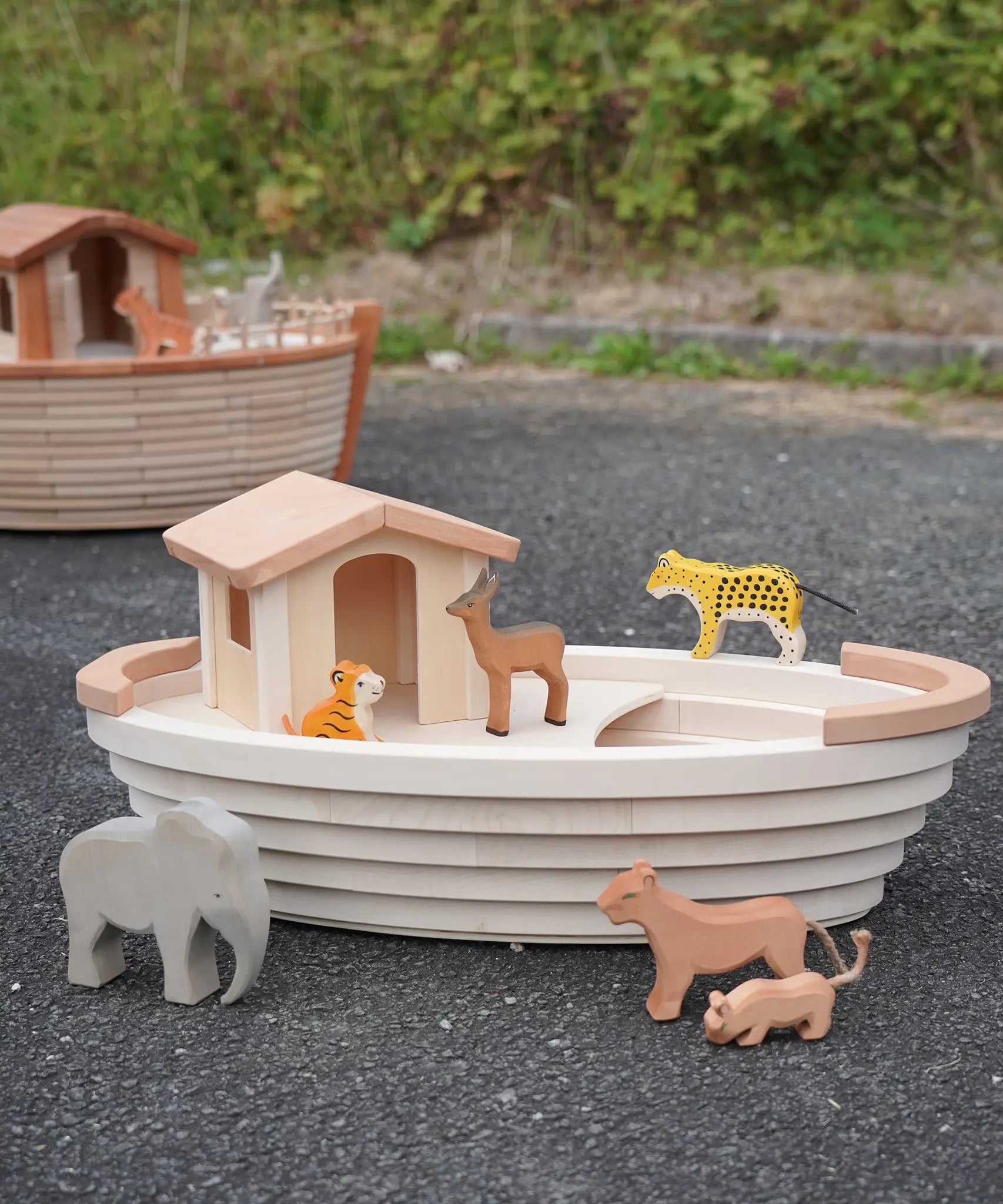 Holztiger handcrafted wooden Noah's ark with different animals on top and a XL ark in the background