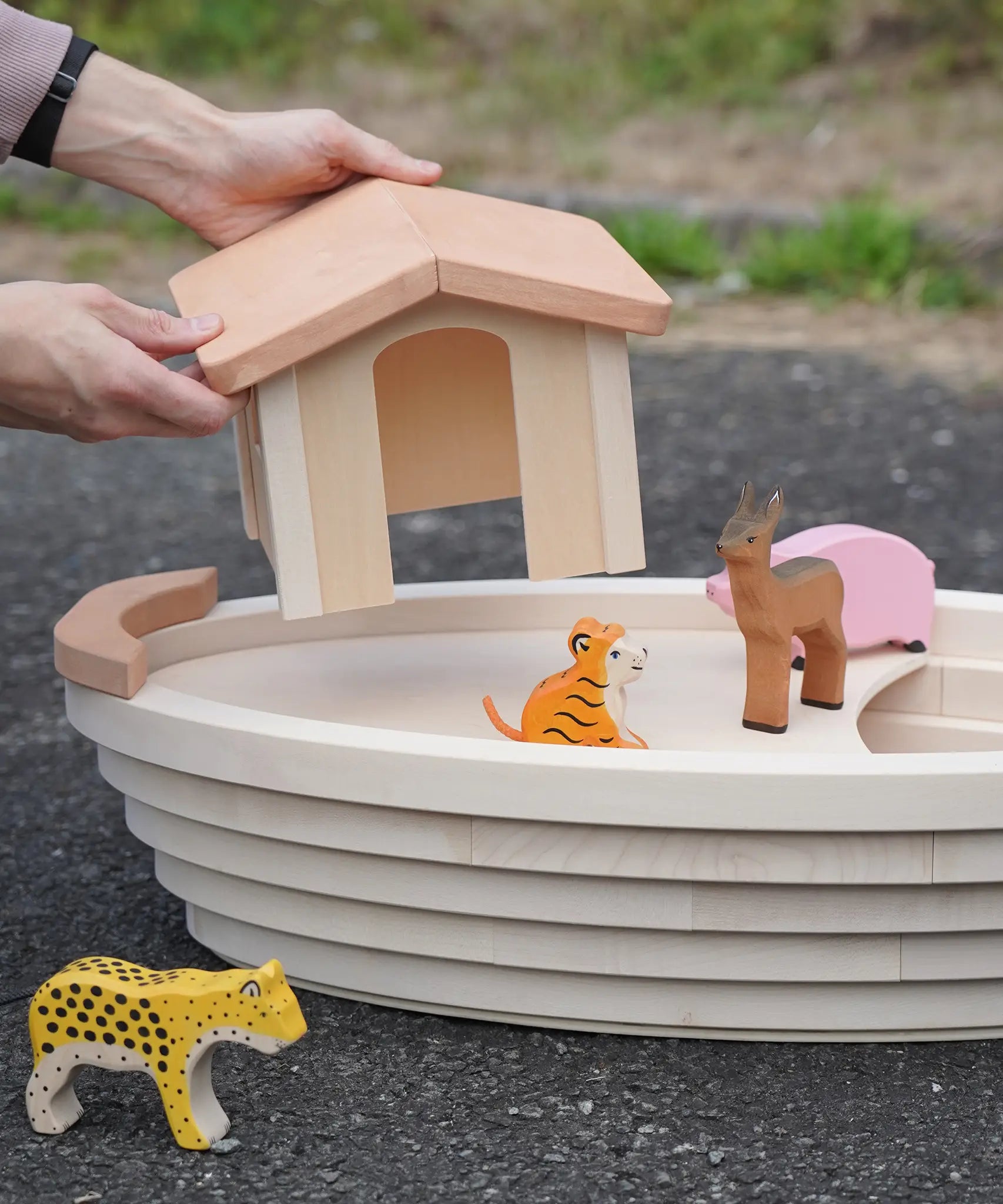 Adult placing the detachable cabin on top of the removable lid on the Holztiger Noah's ark showing animal figures surrounding the ark