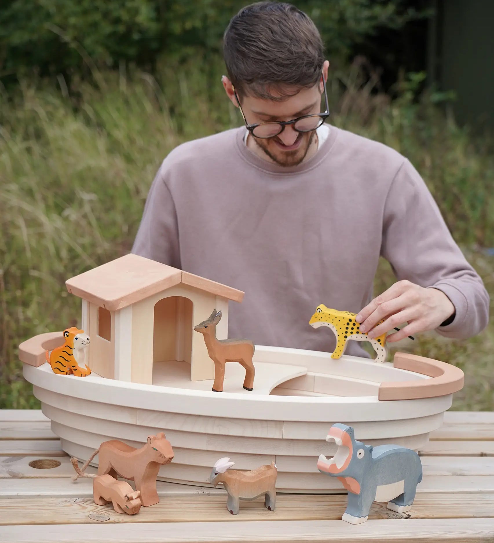 Adult holding a tiger figure on top of a Holztiger handcrafted wooden Noah's ark with other animals 