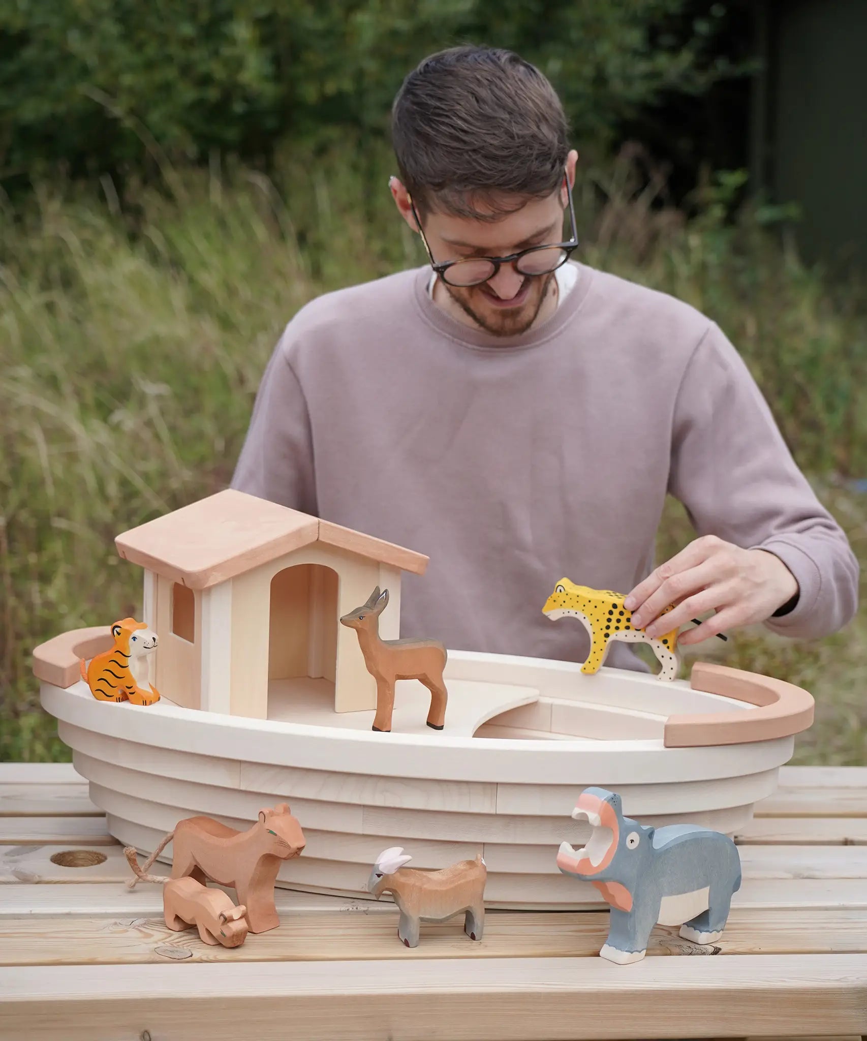 Adult holding a tiger figure on top of a Holztiger handcrafted wooden Noah's ark with other animals 