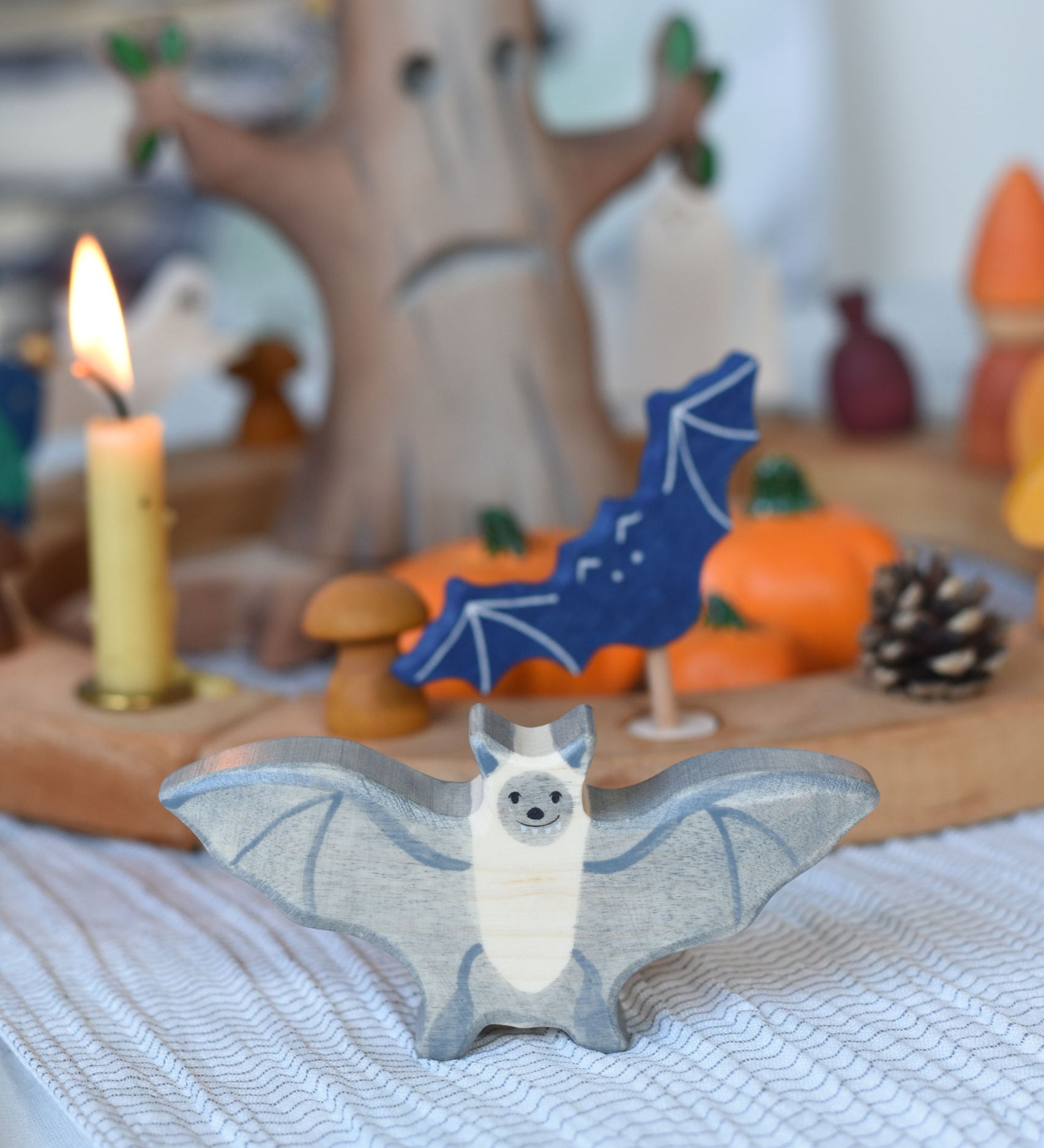 A Holztiger wooden bat toy figure placed on a striped tablecloth in front of a Halloween themed Grimm's celebration ring set up.
This wooden toy figure is part of a wide range of Holztiger figures and scenery perfect for small world play available here at Babipur 