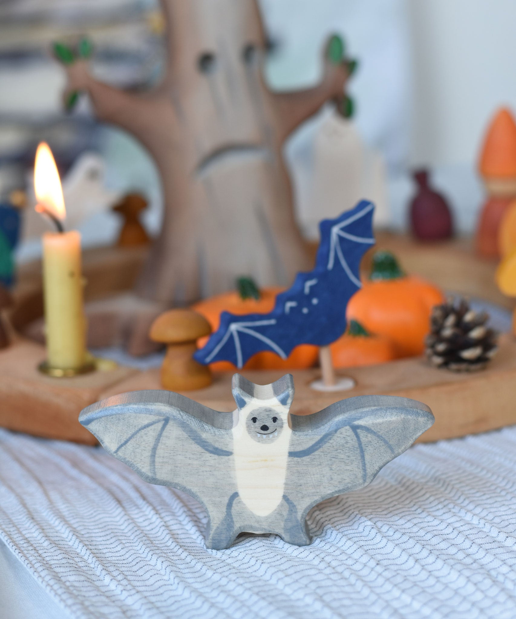 A Holztiger wooden bat toy figure placed on a striped tablecloth in front of a Halloween themed Grimm's celebration ring set up.
This wooden toy figure is part of a wide range of Holztiger figures and scenery perfect for small world play available here at Babipur 