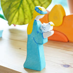 Holztiger Noah's Wife figure with dove placed on a wooden window shelf. A green leaf and a Grimm's sun toy can be seen in the background