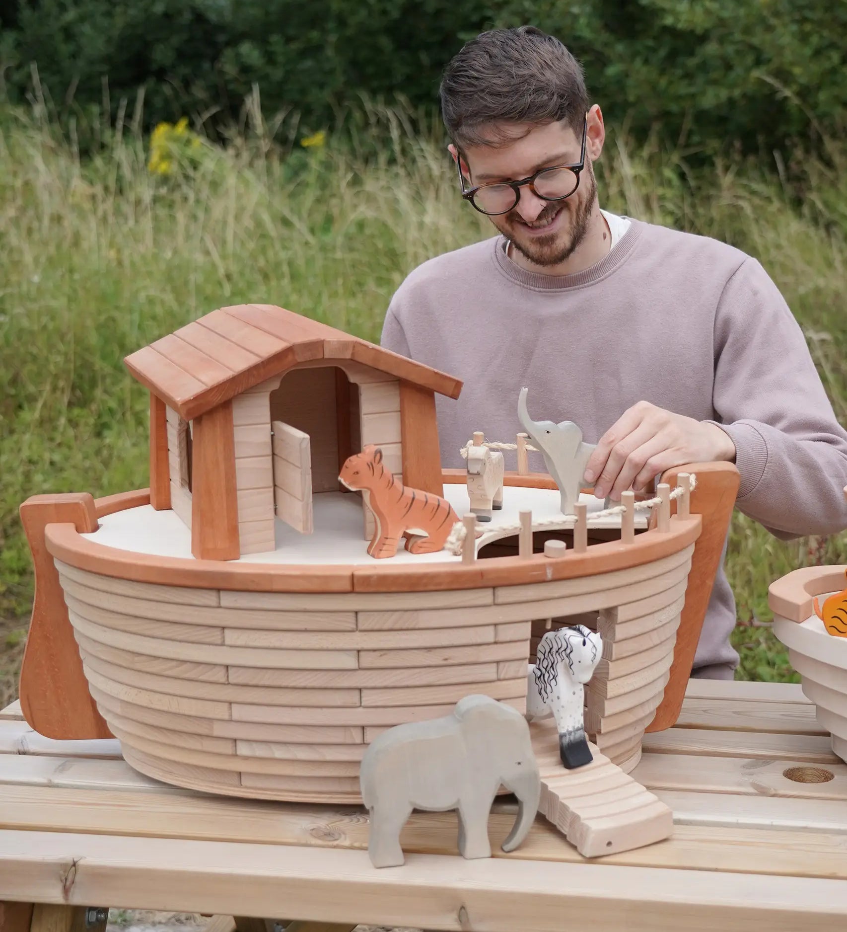 Adult playing with different animal figures on the Holztiger handcrafted XL Noah's ark showing the side ramp down