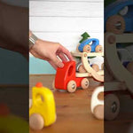 Close up of hand playing with the Bajo wooden transporter lorry toy on a wooden table