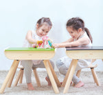 Two children sitting on PlanToys wooden chairs in front of PlanToys wooden desks.