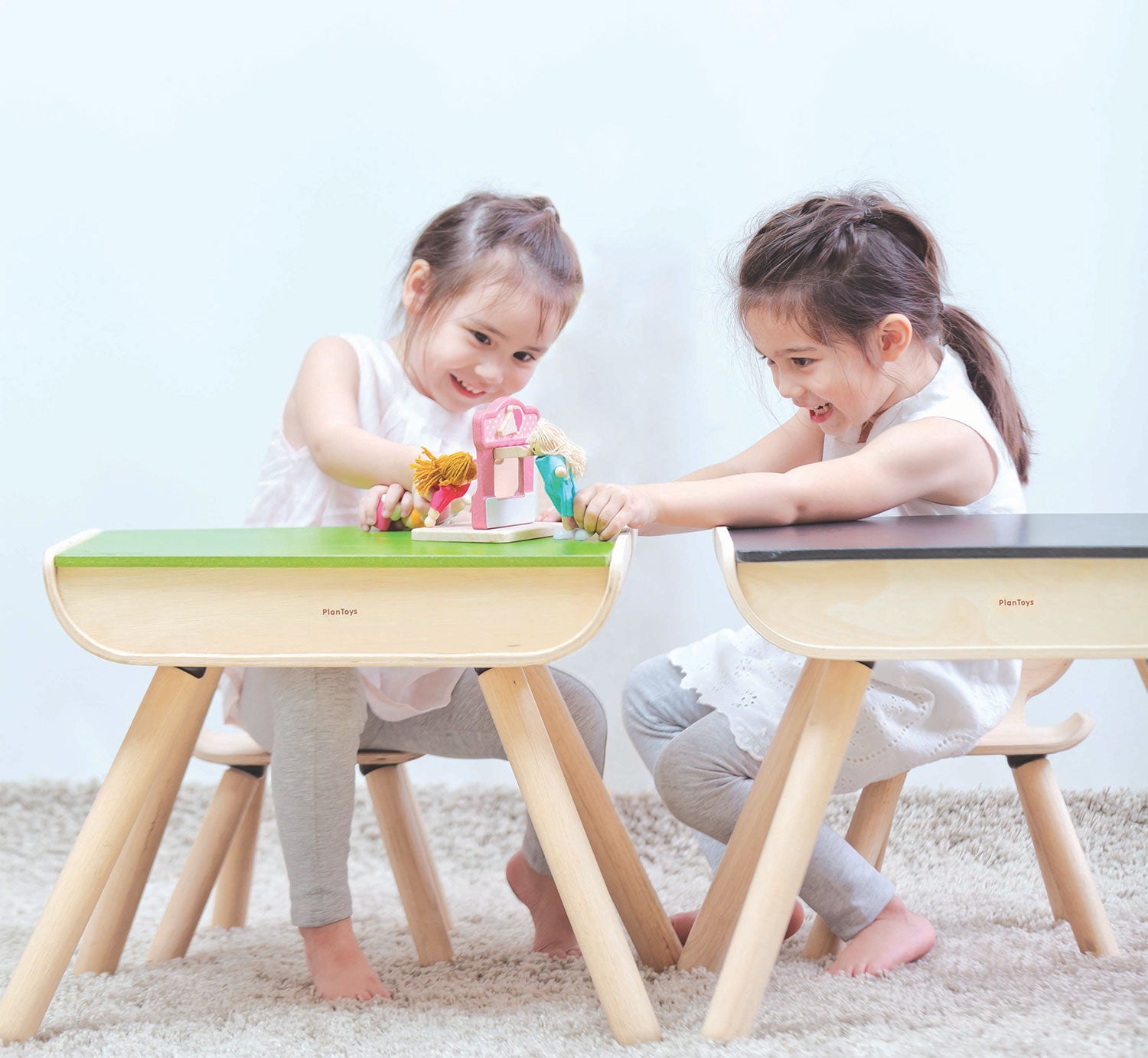 Two children sitting on PlanToys wooden chairs in front of PlanToys wooden desks.