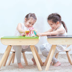 Two children sitting on PlanToys wooden chairs in front of PlanToys wooden desks.