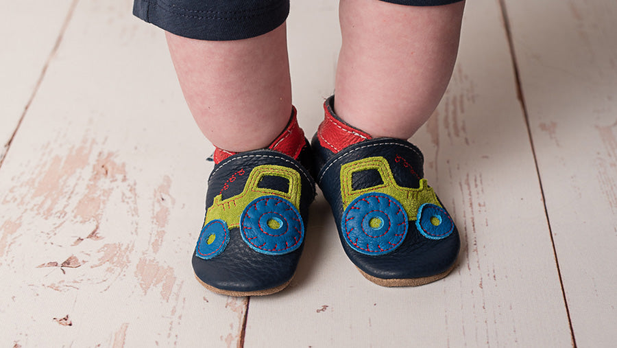 Baby feet wearing a pair of Inch Blue barefoot leather baby shoes with embroidered tractors