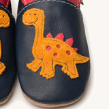A close up of the Inch Blue navy dino baby shoes available at Babipur showing the orange suede dino cut out design