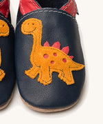 A close up of the Inch Blue navy dino baby shoes available at Babipur showing the orange suede dino cut out design