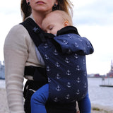  A mother carrying a baby in a anchor Integra carrier available at Babipur. A navy carrier with a all over anchor print. Features a small hood for head protection.
