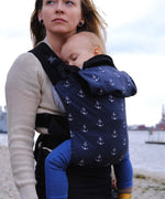  A mother carrying a baby in a anchor Integra carrier available at Babipur. A navy carrier with a all over anchor print. Features a small hood for head protection.