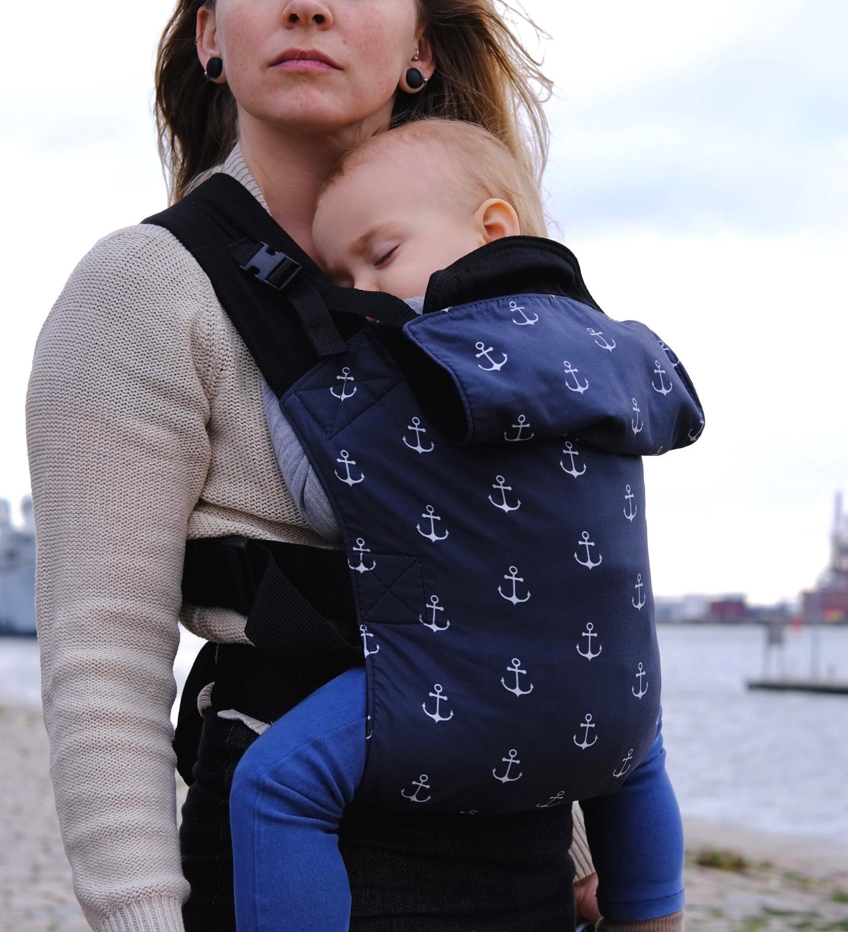  A mother carrying a baby in a anchor Integra carrier available at Babipur. A navy carrier with a all over anchor print. Features a small hood for head protection.