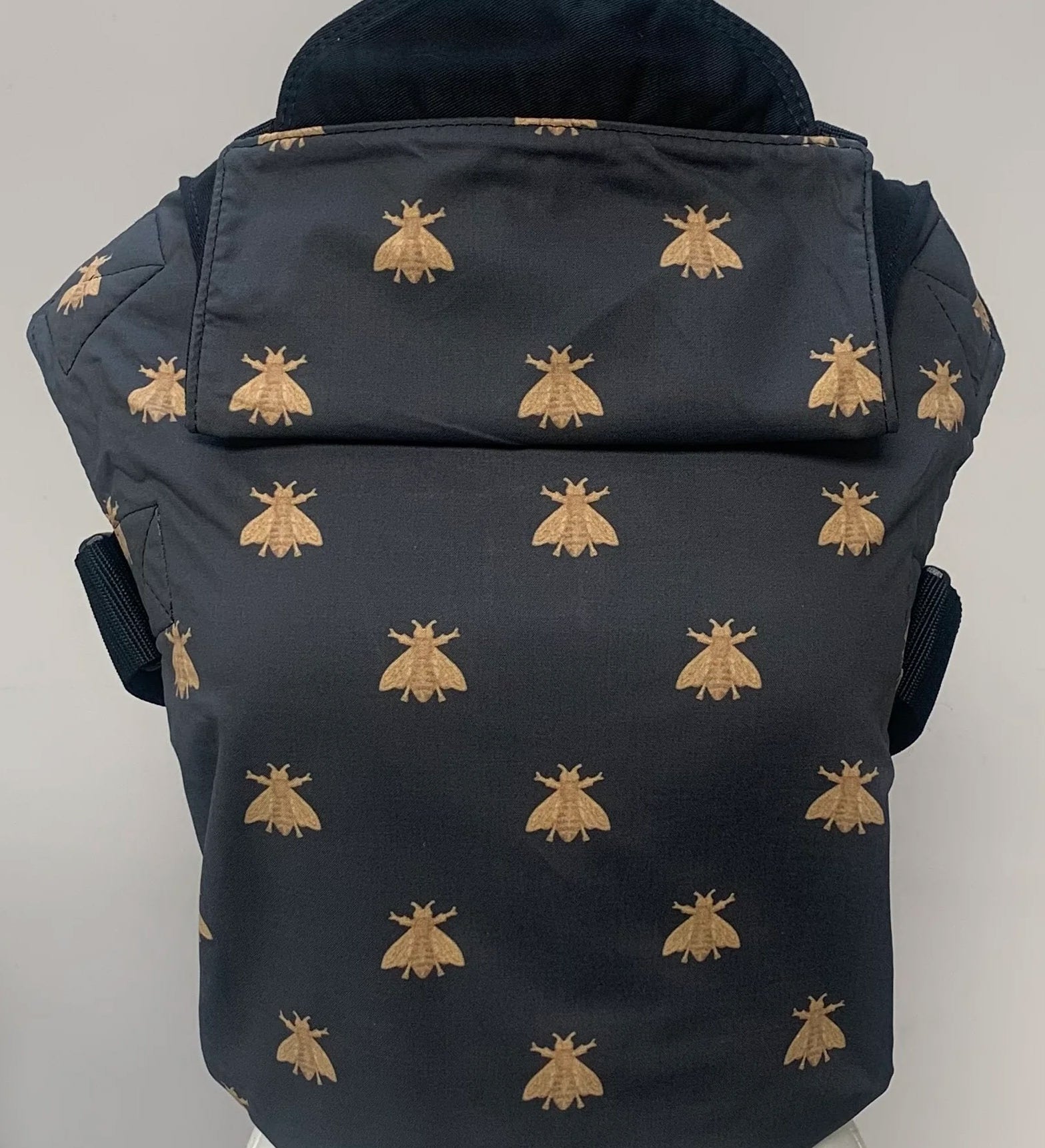 Integra bee design baby carrier available at a Babipur.  A navy carrier with a golden bee design. Features a small hood for head protection.