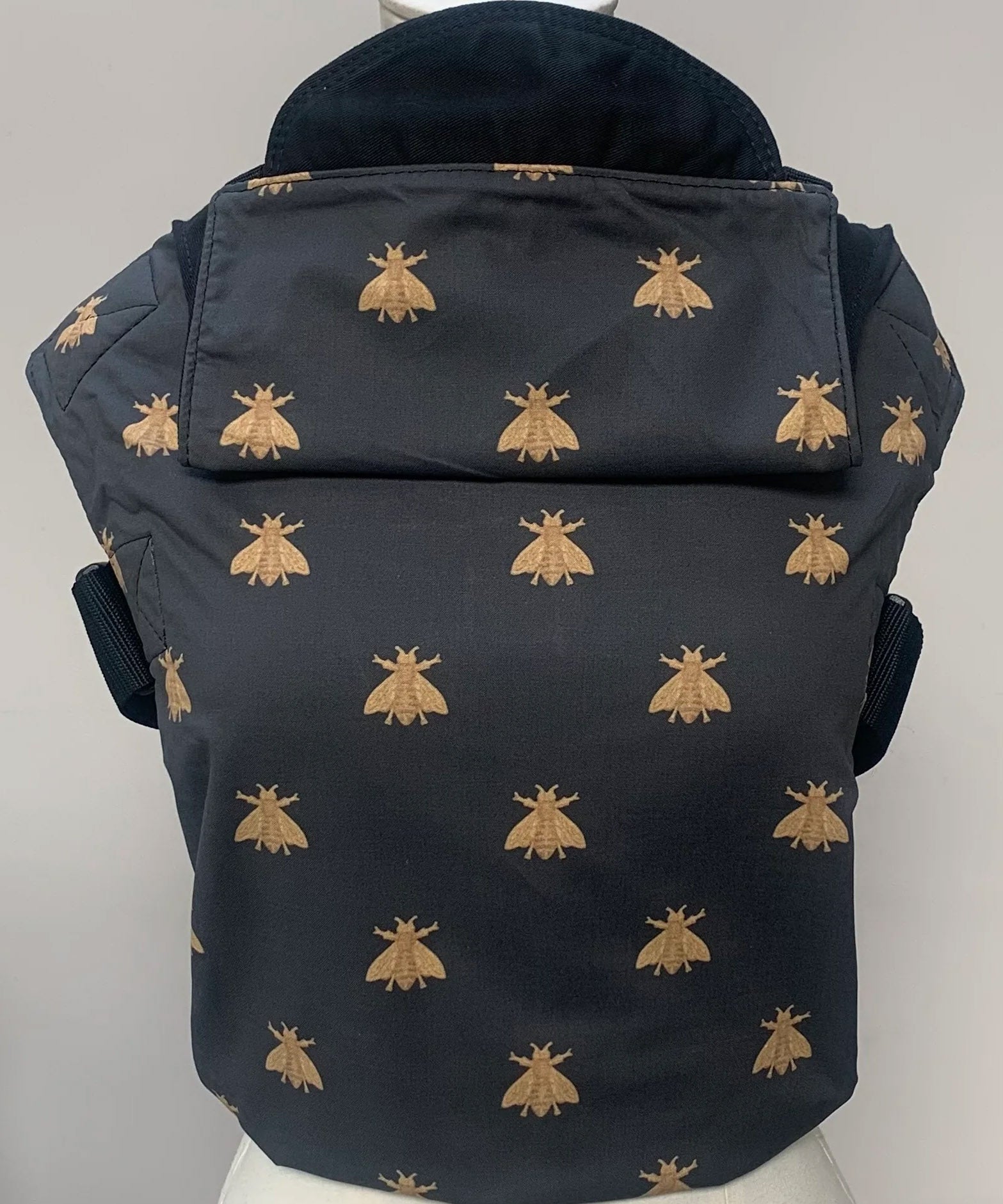 Integra bee design baby carrier available at a Babipur.  A navy carrier with a golden bee design. Features a small hood for head protection.