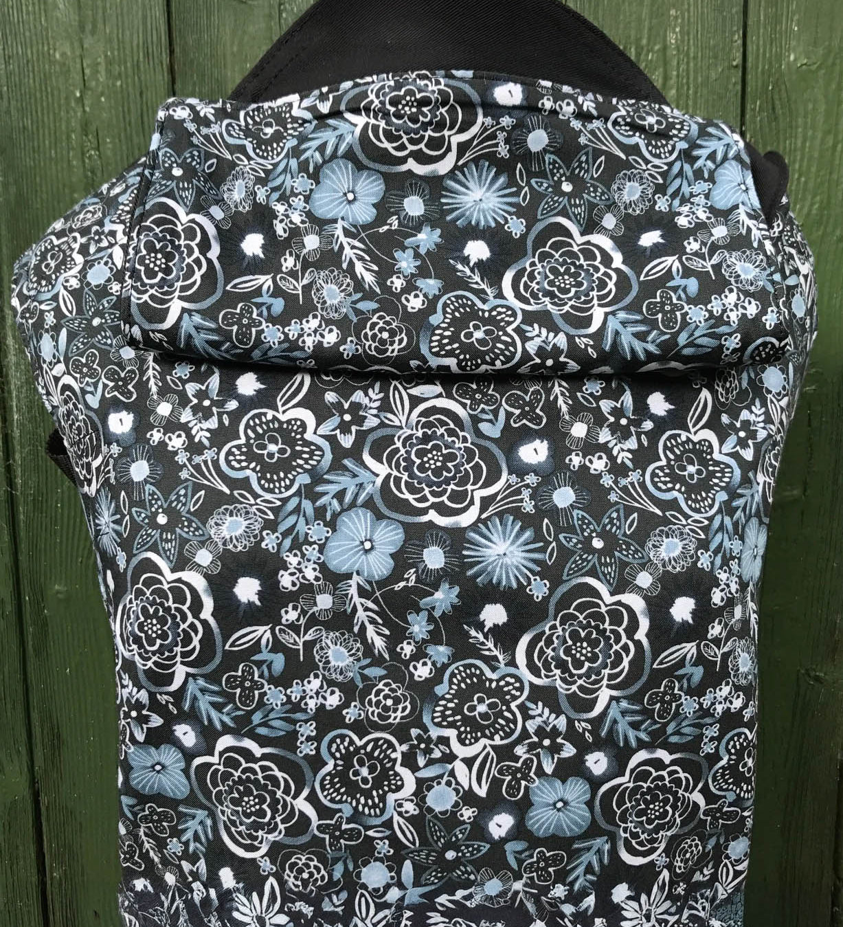 Integra Copenhagen baby carrier available at a Babipur a dark coloured carrier with a white flower design. Features a small hood for head protection.