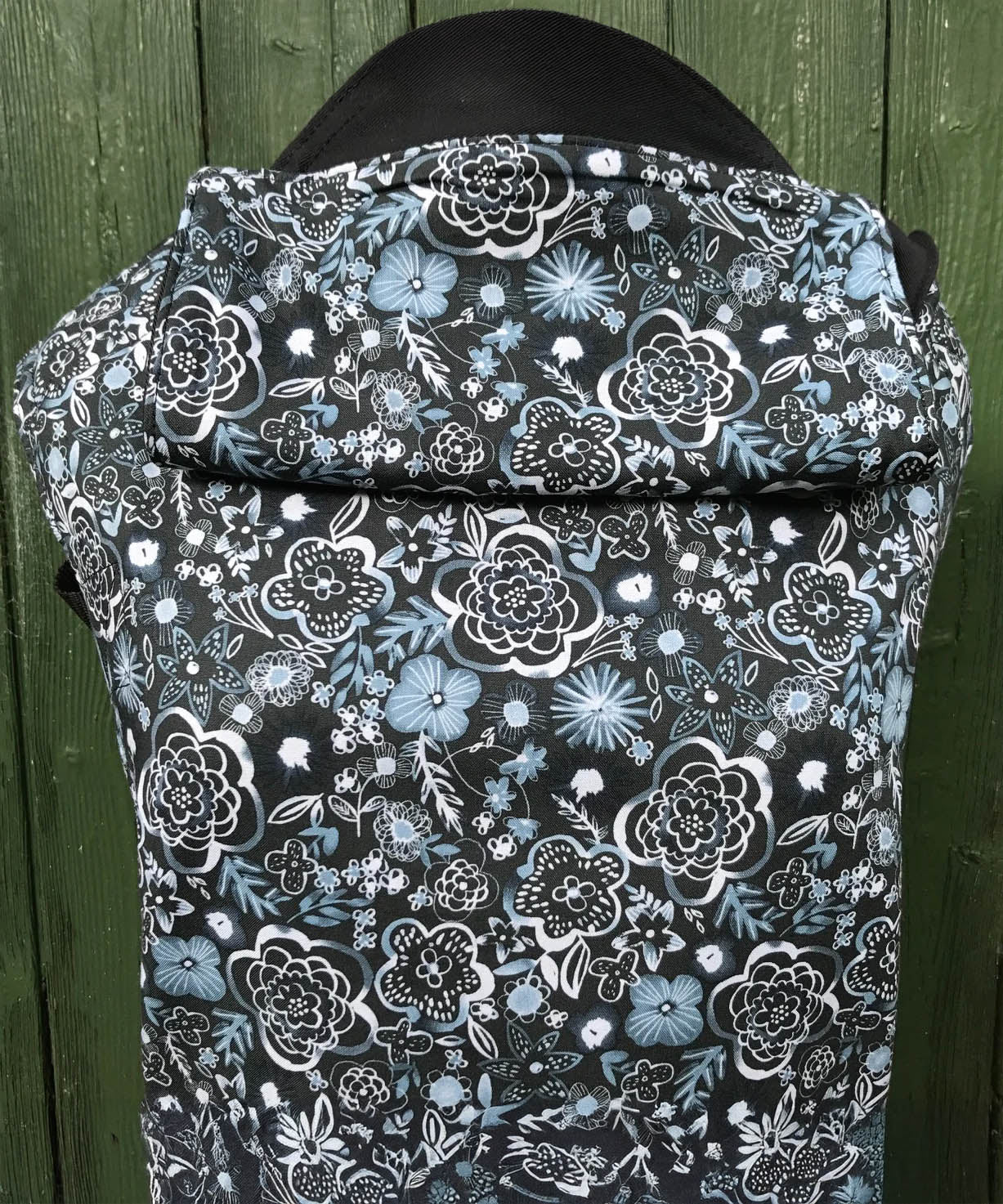 Integra Copenhagen baby carrier available at a Babipur a dark coloured carrier with a white flower design. Features a small hood for head protection.