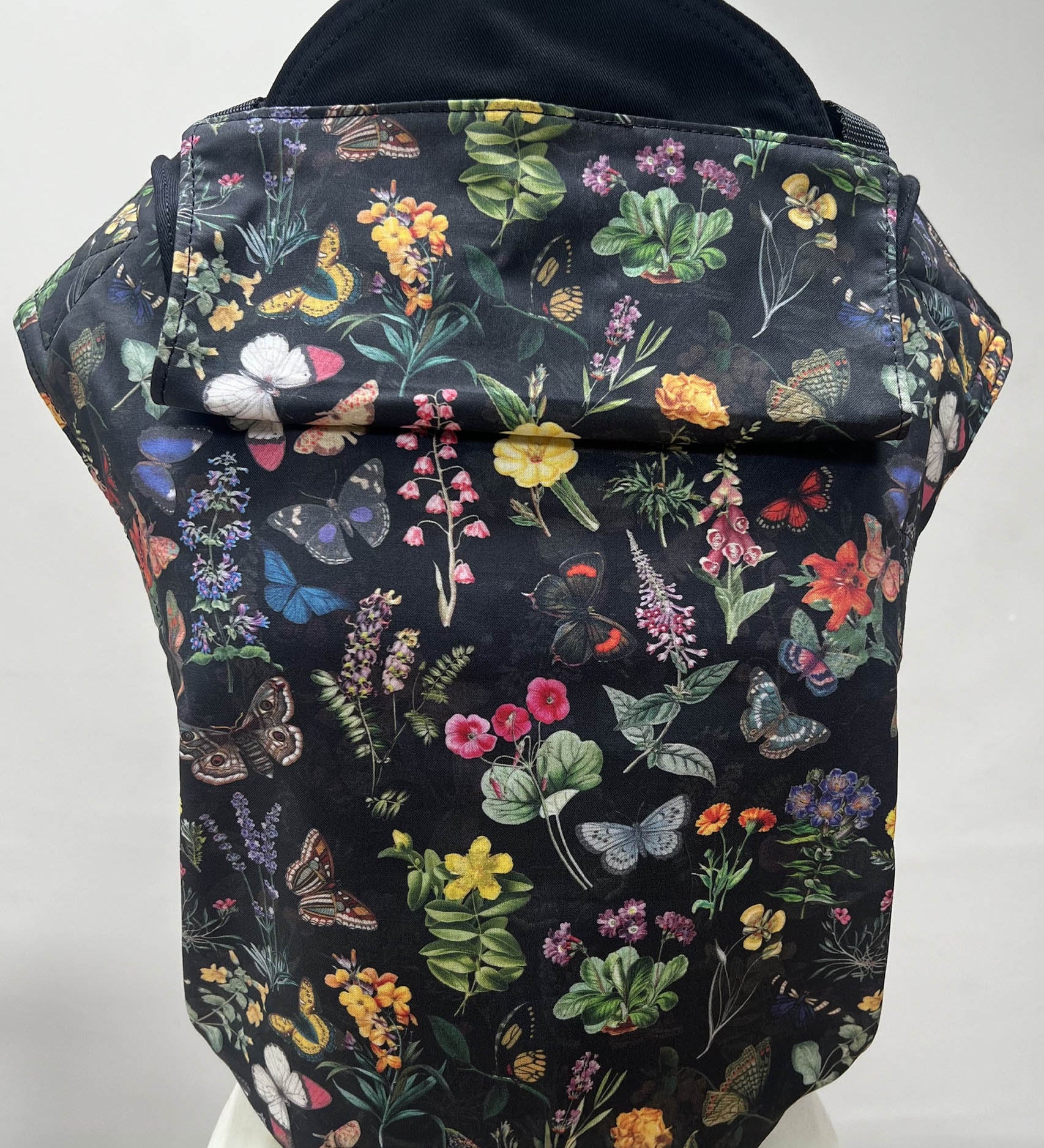 Integra flower garden baby carrier available at a Babipur a dark coloured carrier with a vintage inspired flower and butterfly design. Features a small hood for head protection.