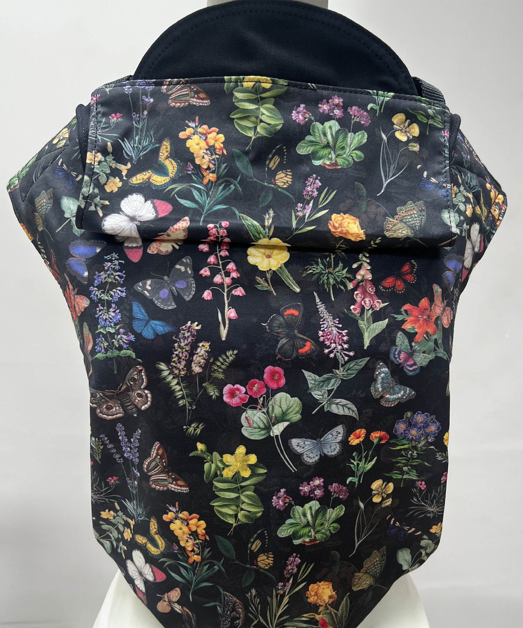 Integra flower garden baby carrier available at a Babipur a dark coloured carrier with a vintage inspired flower and butterfly design. Features a small hood for head protection.