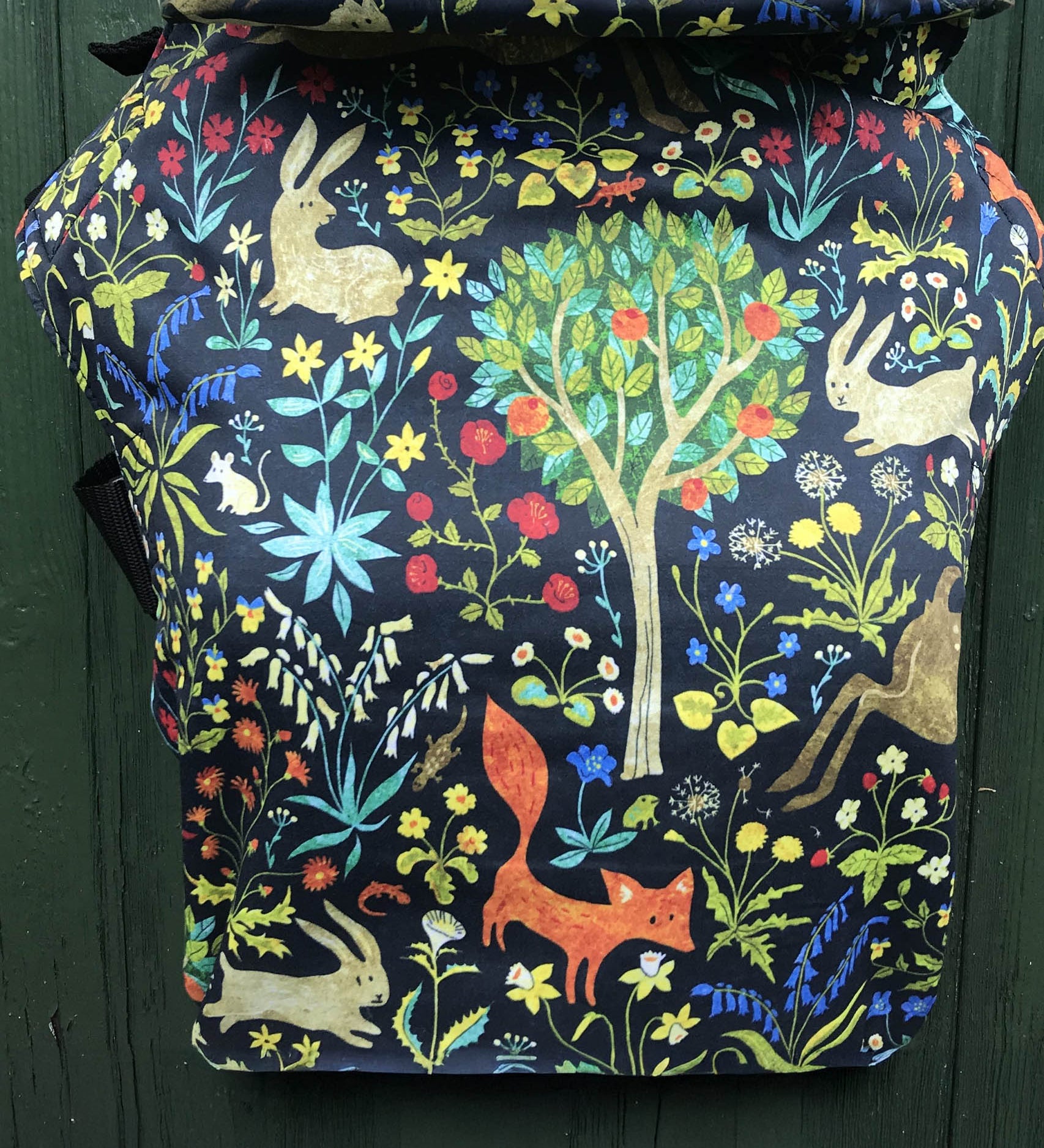 Integra frolic baby carrier available at a Babipur a dark coloured carrier with a playful design of a rabbit fox and various flowers. Features a small hood for head protection.