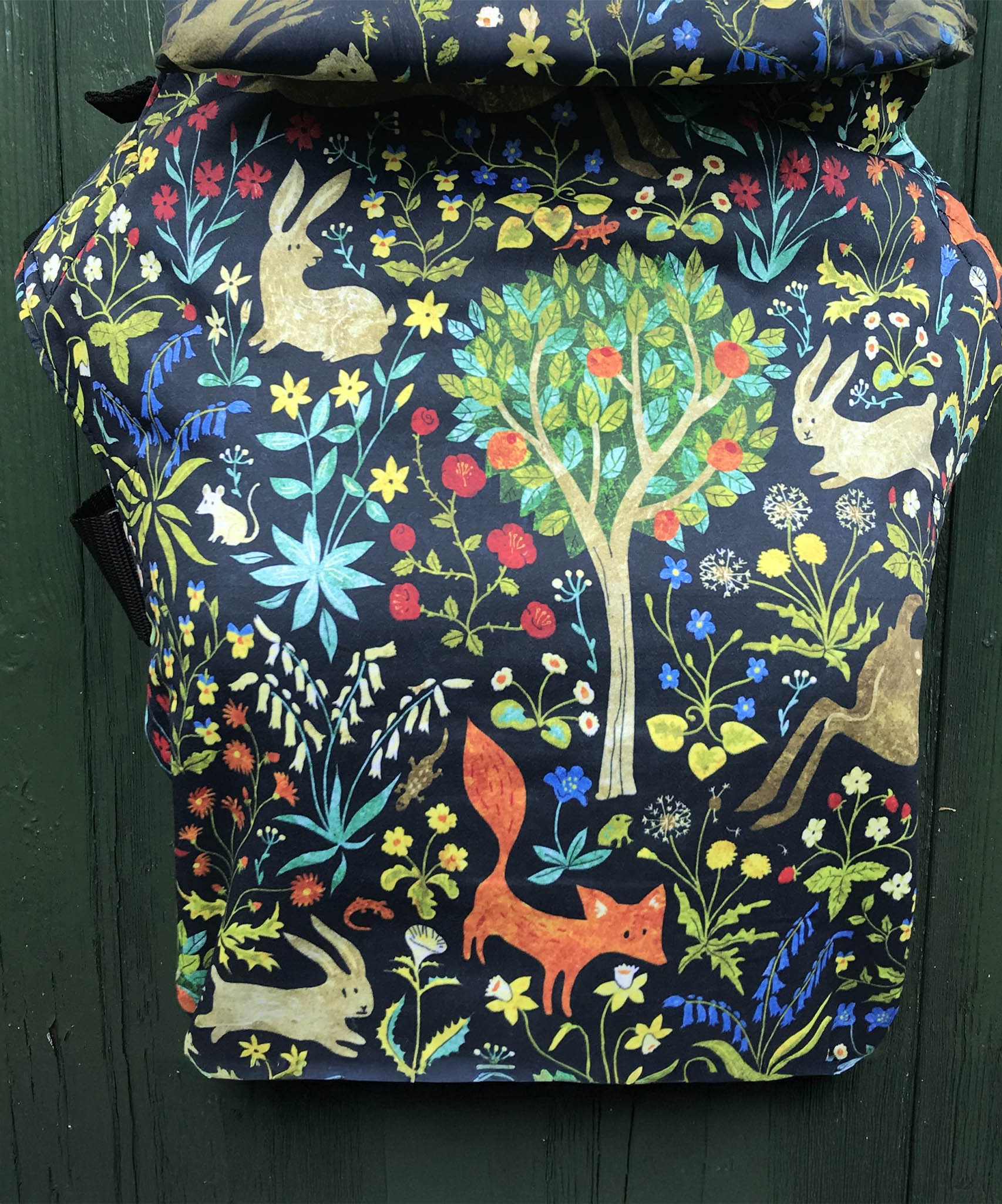 Integra frolic baby carrier available at a Babipur a dark coloured carrier with a playful design of a rabbit fox and various flowers. Features a small hood for head protection.