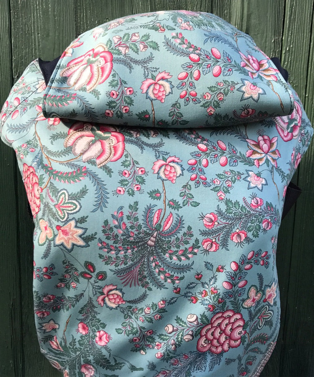 Integra Martha baby carrier available at a Babipur a light blue coloured carrier with a vintage pink floral design. Features a small hood for head protection.