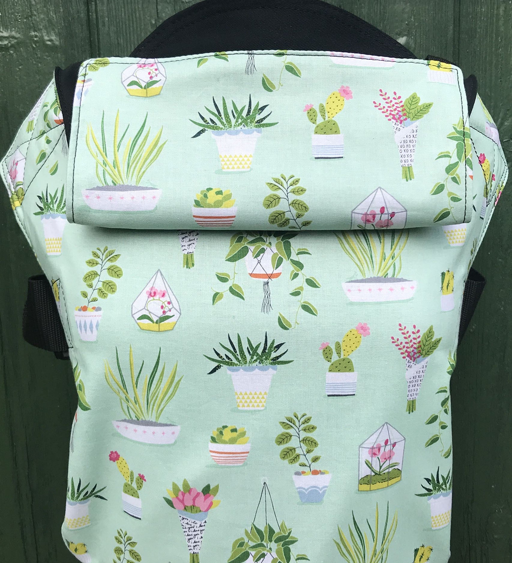 Integra viva baby carrier available at a Babipur a lightly coloured carrier with green house plants prints. Features a small hood for head protection.