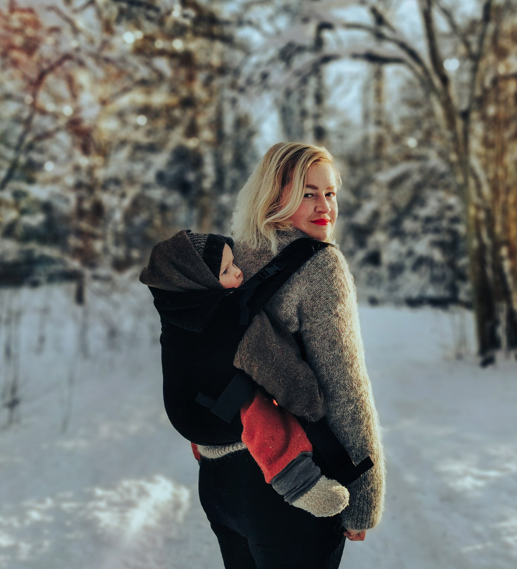 A mother carrying a baby outside in the Integra baby carrier in essential black available at Babipur.