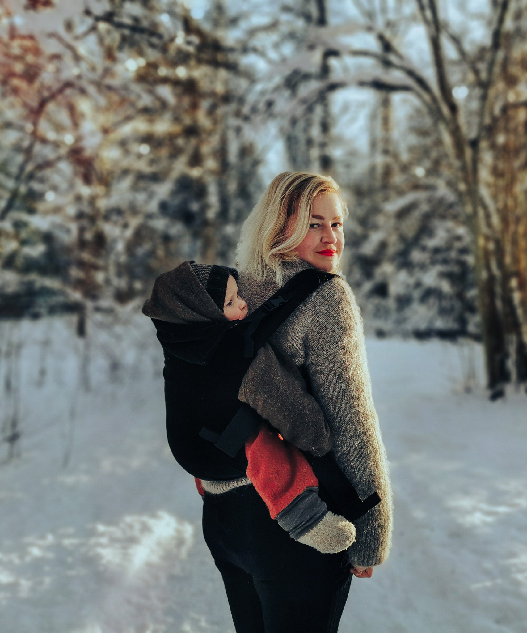 A mother carrying a baby outside in the Integra baby carrier in essential black available at Babipur.