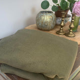 A close up of the Integra khaki texture linen baby carrier available at a Babipur Showing the carrier folded up on a wooden table