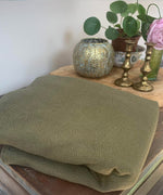 A close up of the Integra khaki texture linen baby carrier available at a Babipur Showing the carrier folded up on a wooden table