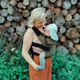 A mother carrying a baby outdoors in the Integra khaki texture linen baby carrier available at a Babipur. 