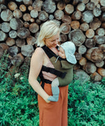 A mother carrying a baby outdoors in the Integra khaki texture linen baby carrier available at a Babipur. 