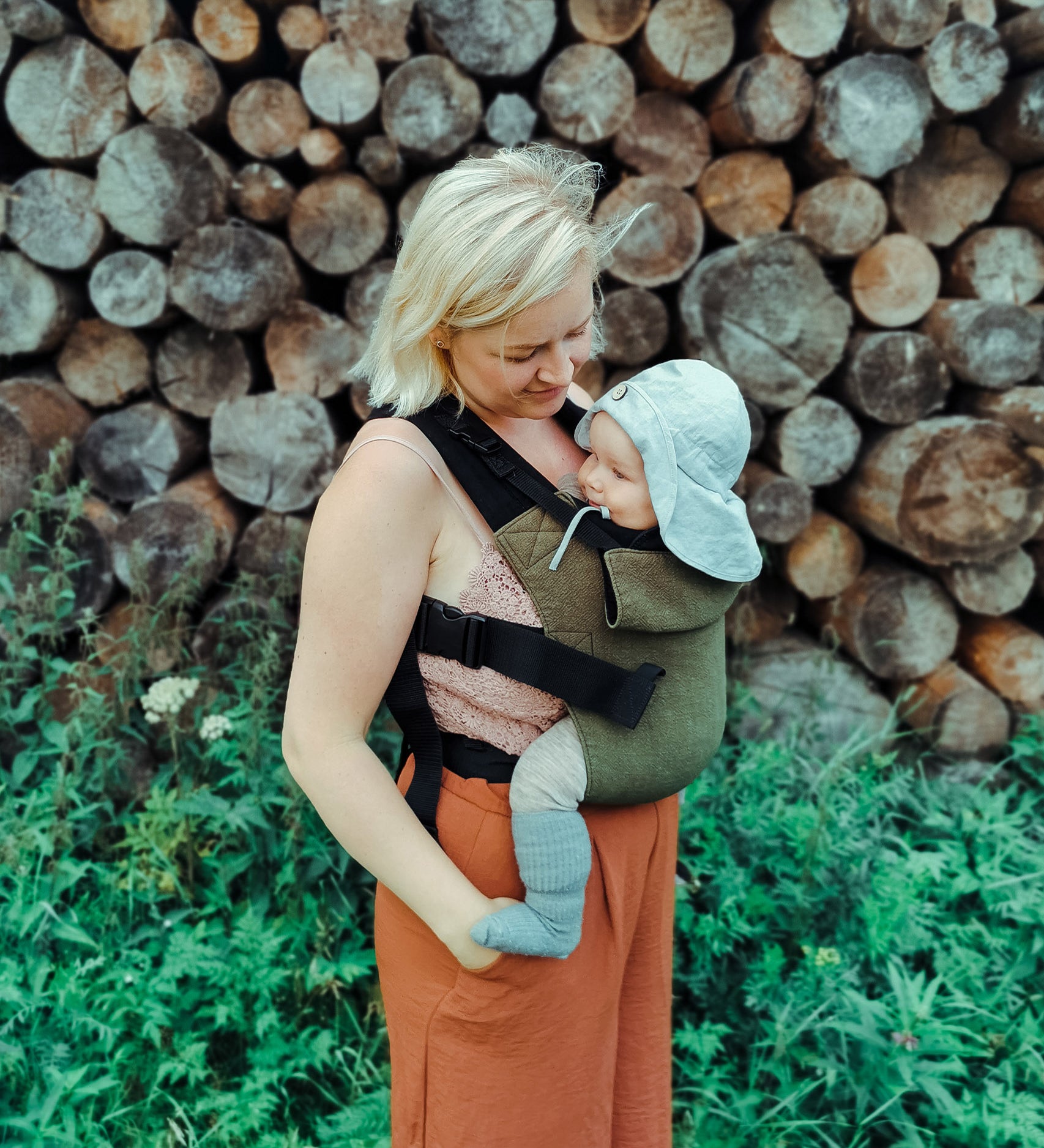 A mother carrying a baby outdoors in the Integra khaki texture linen baby carrier available at a Babipur. 