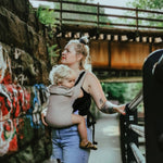 A person wearing the Integra Size 3 Taupe Regular Strap Baby Carrier whilst walking outside
