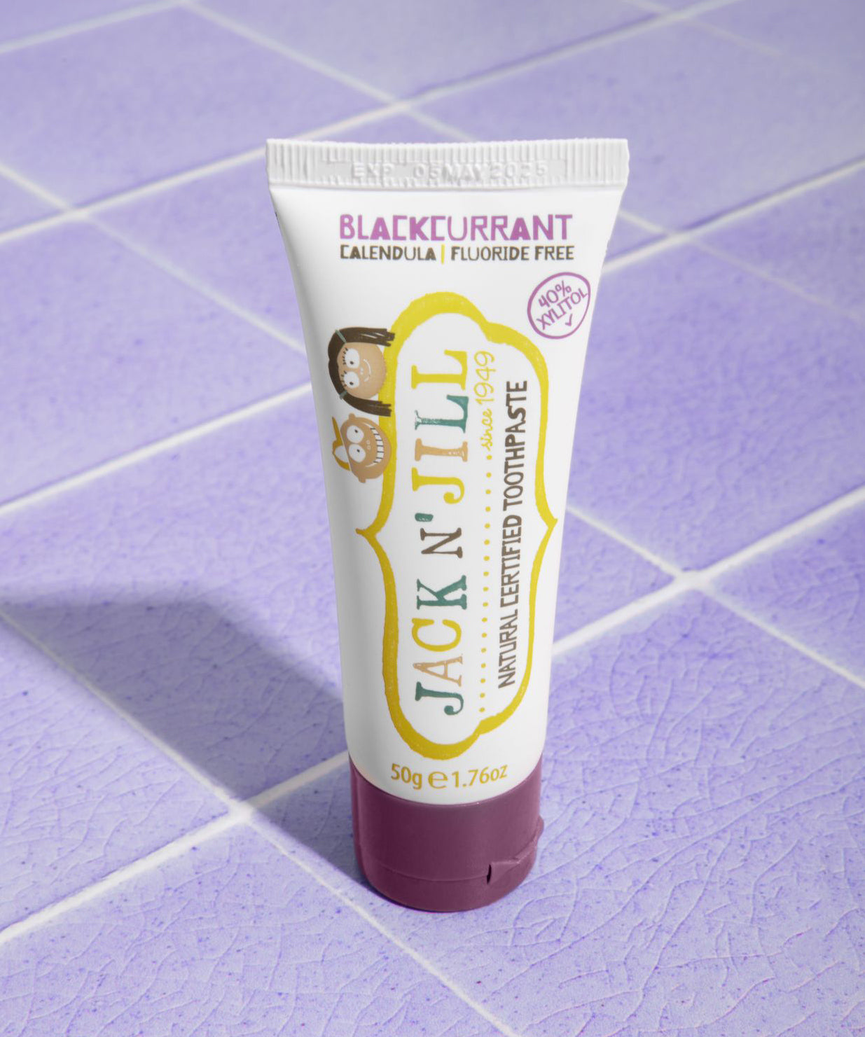 A 50g tube of Jack N' Jill blackcurrant flavoured fluoride free kid's toothpaste placed on a purple coloured tiled surface.