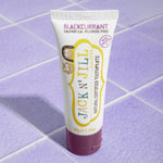 A 50g tube of Jack N' Jill blackcurrant flavoured fluoride free kid's toothpaste placed on a purple coloured tiled surface.