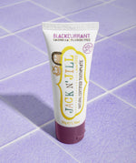 A 50g tube of Jack N' Jill blackcurrant flavoured fluoride free kid's toothpaste placed on a purple coloured tiled surface.