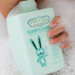 Child holding botttle of Jack N' Jill Blissful Bubbles Bubble Bath with Bubble Wand in their hand covered in bubbles