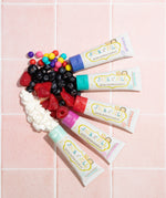 Five tubes of different flavoured Jack n Jill kids natural toothpaste, with fruits and candies to represent their flavours. 