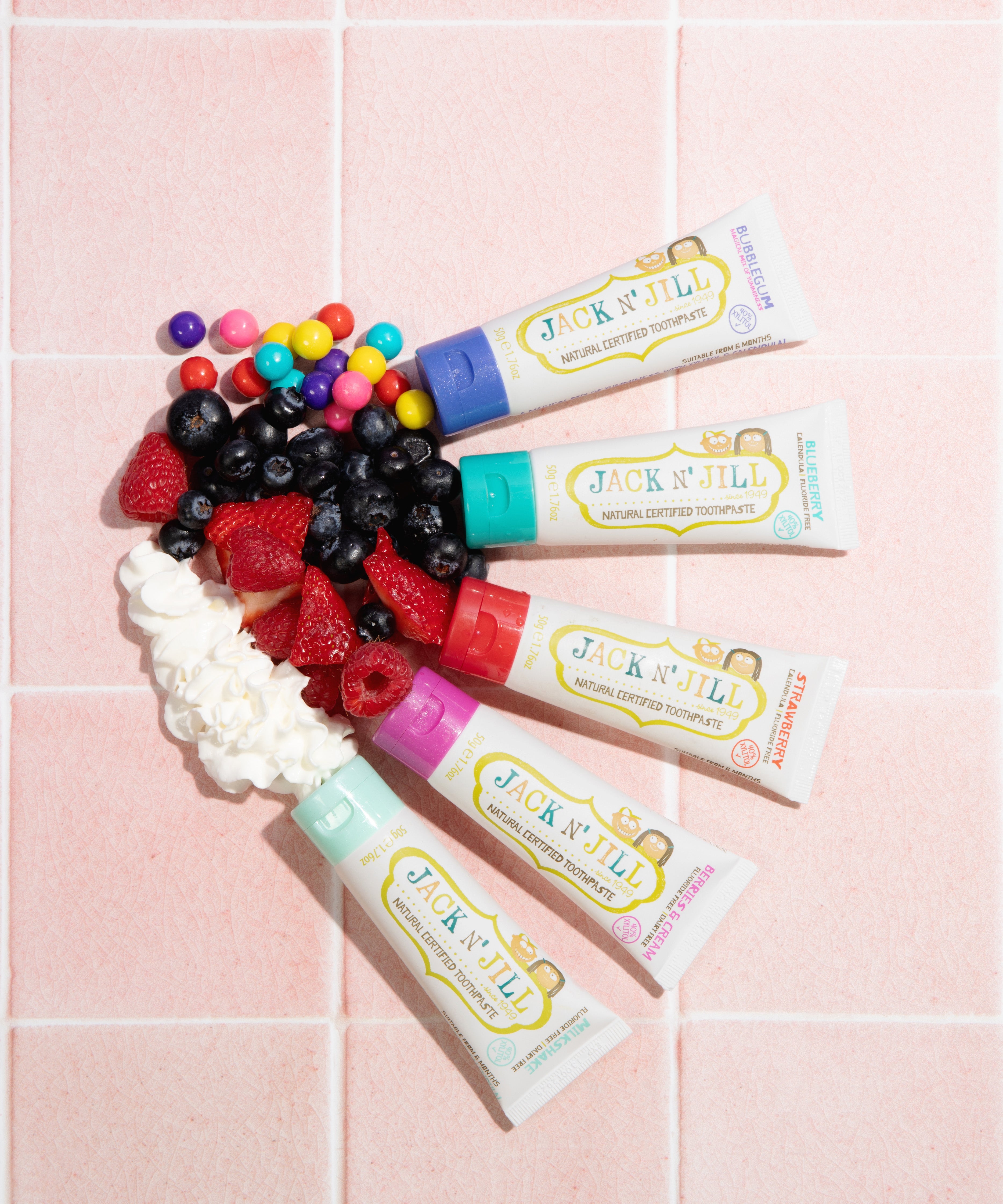 Five tubes of different flavoured Jack n Jill kids natural toothpaste, with fruits and candies to represent their flavours. 