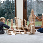 Two children playing with the Just Blocks Smart Lines set stacked in the shape of a big building on a grey carpet