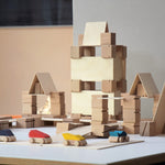 Just Blocks plastic-free wooden Smart Line Blocks stacked into the shape of a building behind some wooden toy cars