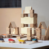 Just Blocks plastic-free wooden Smart Line Blocks stacked into the shape of a building behind some wooden toy cars