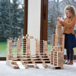 Girl stacking up Just Blocks plastic-free wooden shapes in a large tower on a grey carpet