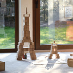 Just Blocks eco-friendly wooden shapes piled into two towers on a grey carpet in front of two large windows