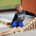 Young boy playing with a wooden ball run made using Just Blocks Smart Lines on a grey carpet