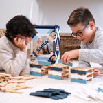 Close up of two boys laying down building towers with the Kapla plastic-free Waldorf toy blocks on a white carpet